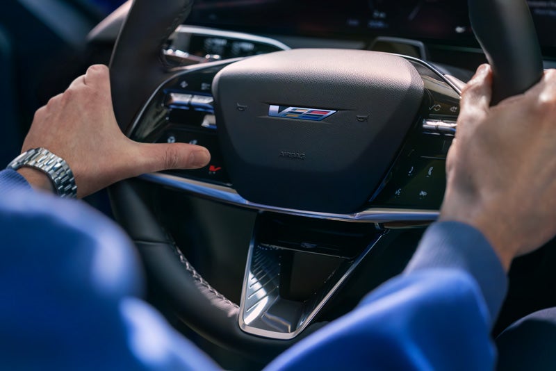 Close-up of a Man About to Press the V-Button on the 2026 OPTIQ-V Steering Wheel | Walker-Jones Cadillac in Waycross GA